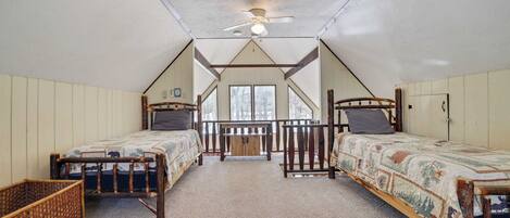 Quarto com duas camas de madeira, um ventilador de teto e vista do exterior através de grandes janelas.