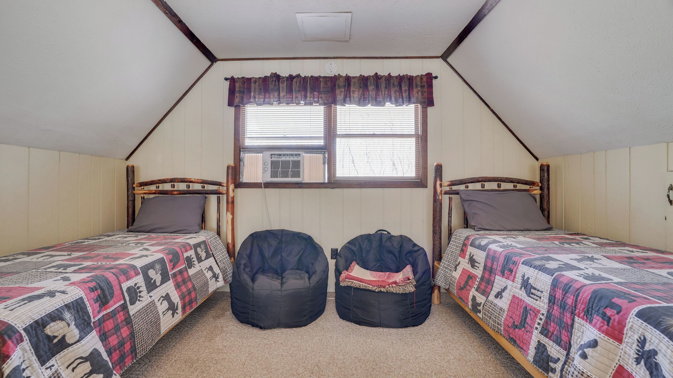 A dormitory room with two beds, a window with blinds, a ceiling vent, and a wall-mounted air conditioning unit.