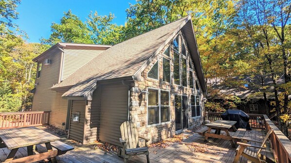 A cabin with a sloped roof, a stone extension, and a deck with picnic tables.
