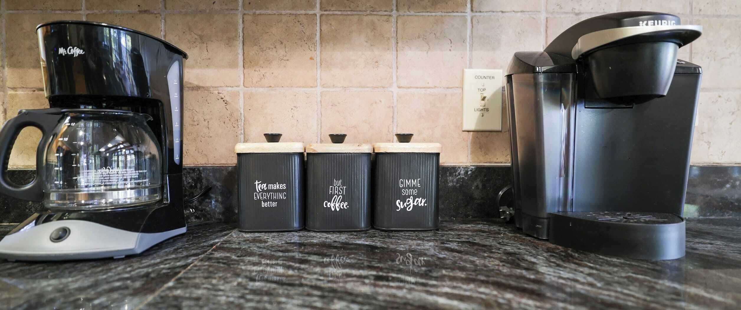 A kitchen counter with a coffee maker, three spice containers, and a Keurig coffee maker.