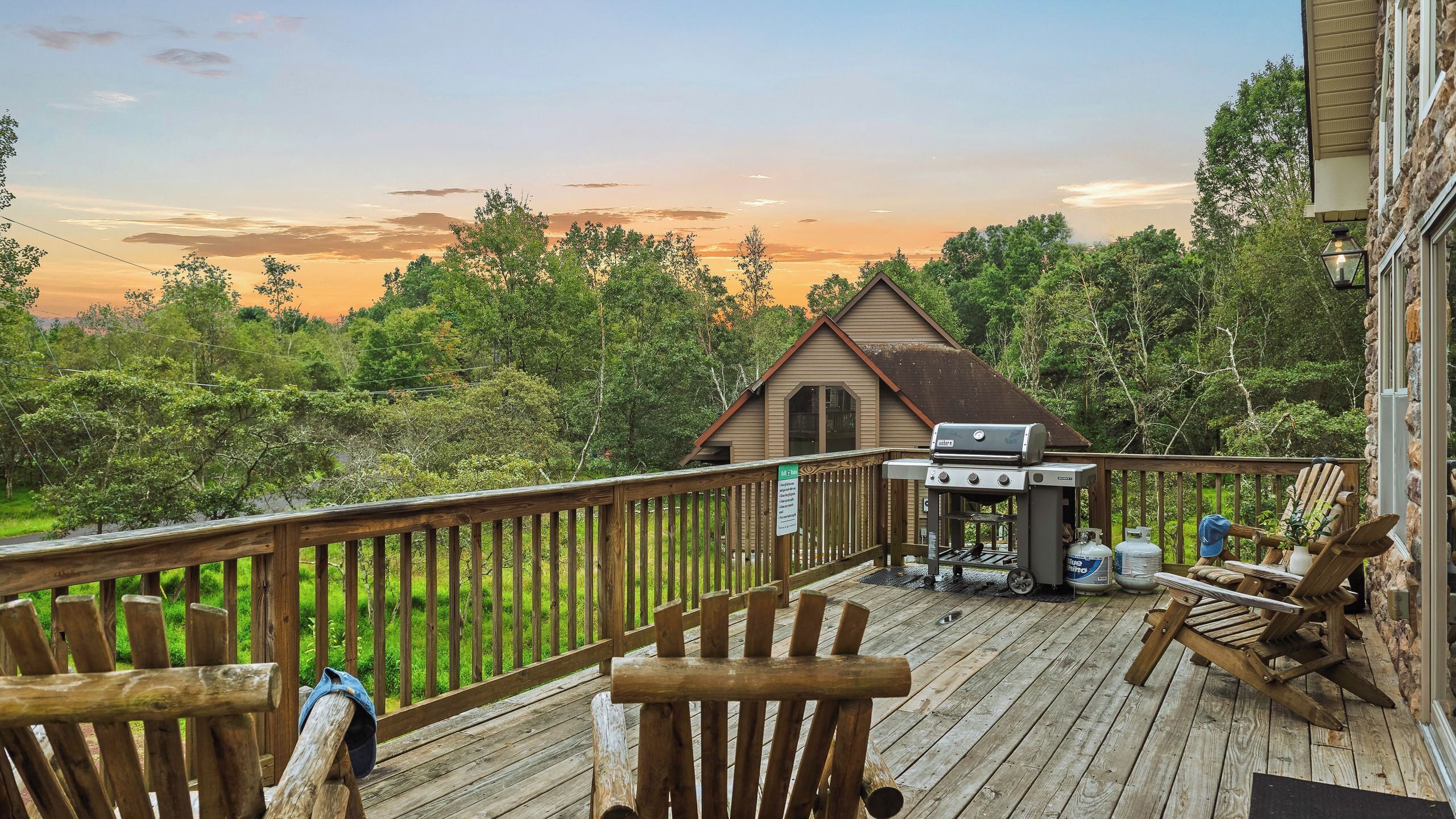 A wooden deck with a barbecue grill, outdoor seating, and a view of a forested area.