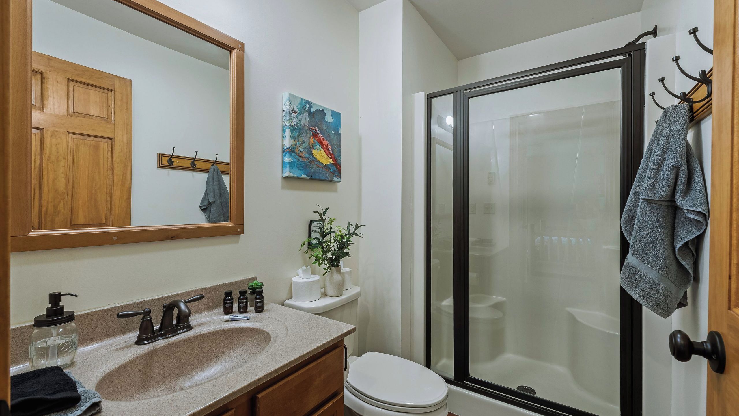 A bathroom with a sink, mirror, toilet, shower, and a towel rack.