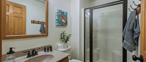 A bathroom with a sink, mirror, toilet, shower, and a towel rack.