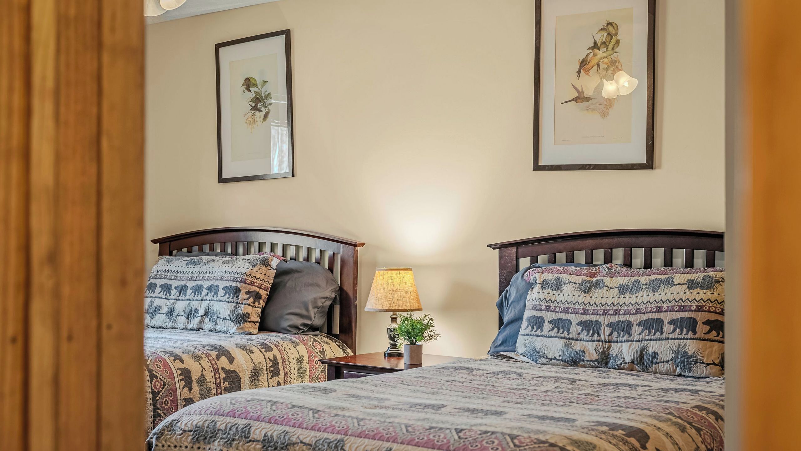 Une chambre avec deux lits, une table de chevet avec une lampe et deux reproductions botaniques encadrées au mur.