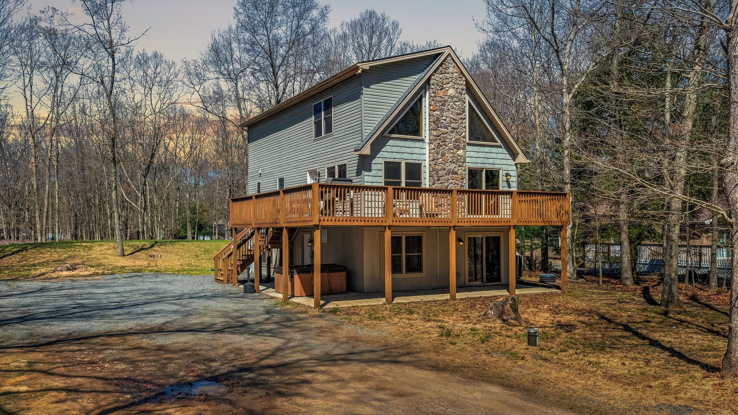 A two-story cabin with a stone accent wall, a wooden deck, and a covered porch.