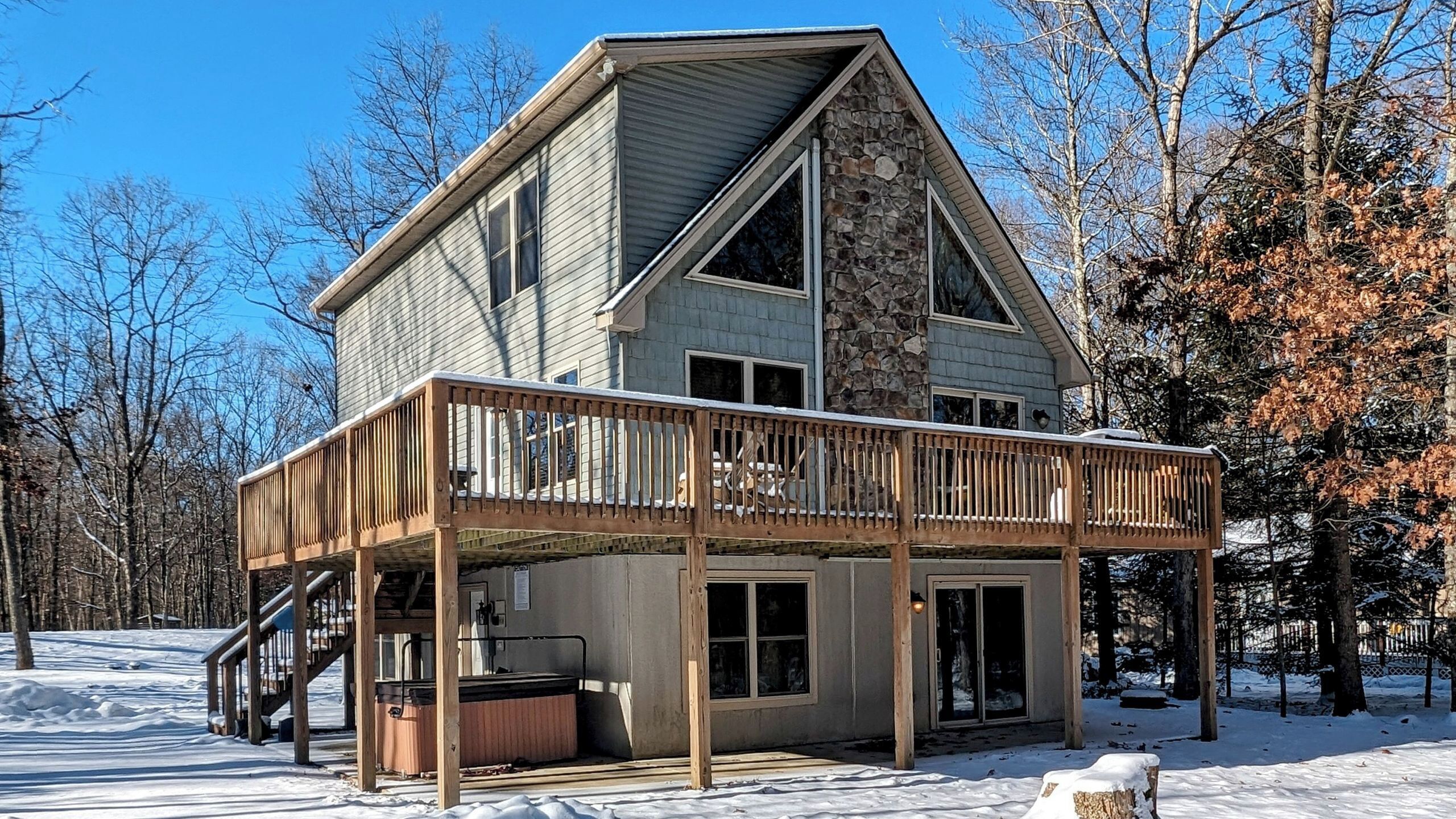 A two-story cabin with a wooden deck, a stone exterior, and a hot tub.