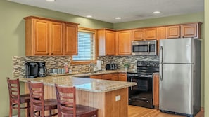 A kitchen with wooden cabinets, a granite countertop, a stainless steel refrigerator, and a built-in microwave.