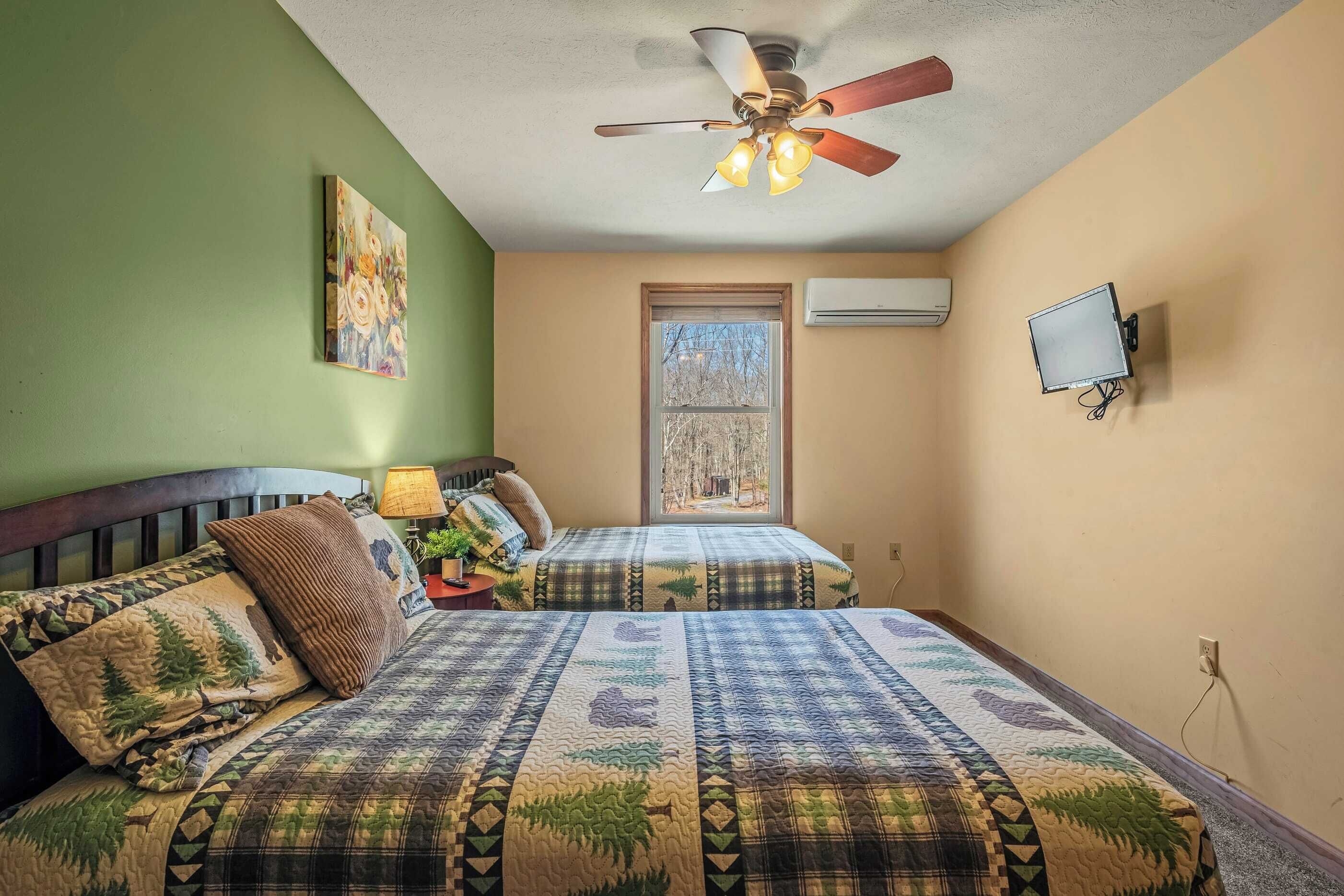 A bedroom with two beds, a ceiling fan, a window, an air conditioner, and a mounted TV.