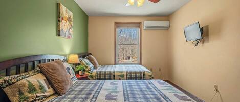 A bedroom with two beds, a ceiling fan, a window, an air conditioner, and a mounted TV.