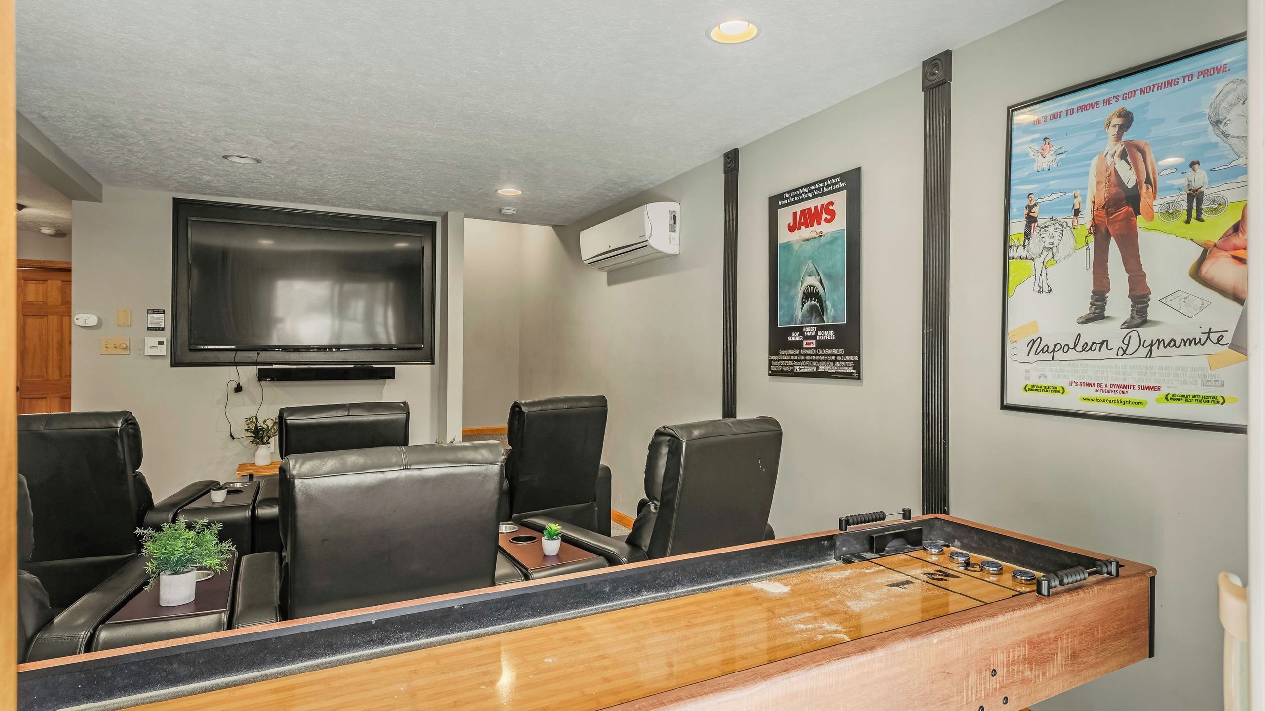A room with a flat-screen TV, air conditioning, posters, and a foosball table.