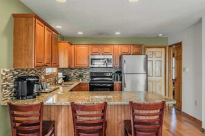 A kitchen with wooden cabinets, a granite countertop, a stainless steel refrigerator, a microwave, and a stove. - Hickory Haven by Avantstay Hot Tub, Game Room, Theater, Deck (Albrightsville)