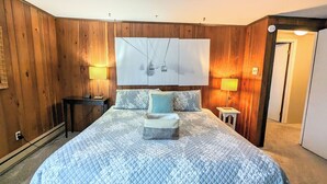 A bedroom with a large bed, two bedside tables, a nightstand, a wall-mounted TV, and wooden paneling.