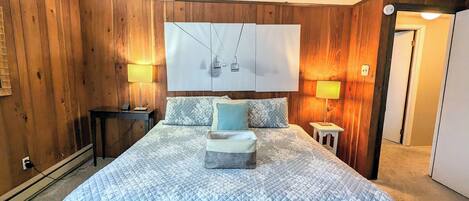 A bedroom with a large bed, two bedside tables, a nightstand, a wall-mounted TV, and wooden paneling.