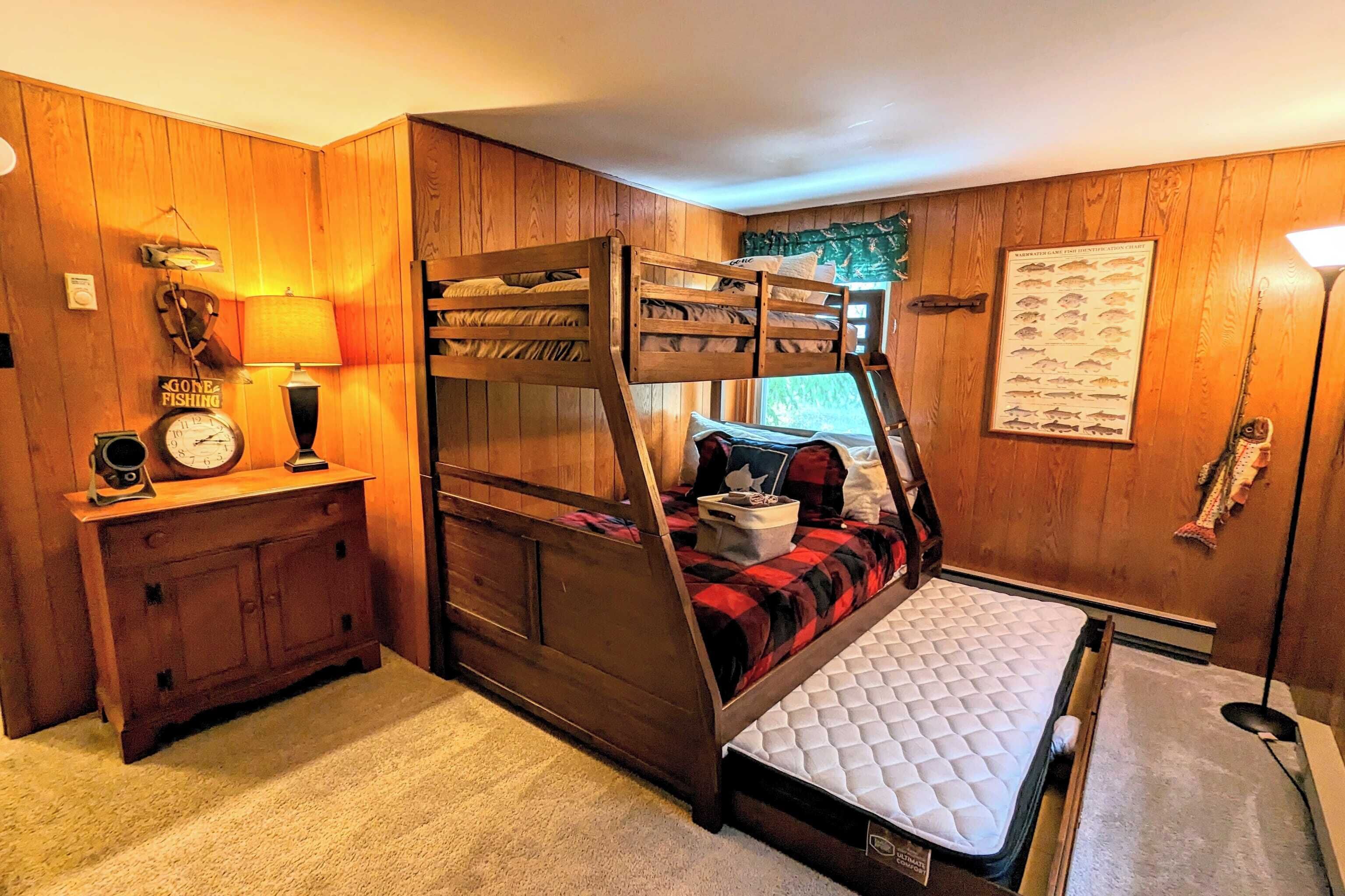 Een stapelbed met een gewatteerde matras, een houten dressoir met een klok, een lamp en een poster met vissen op de muur.