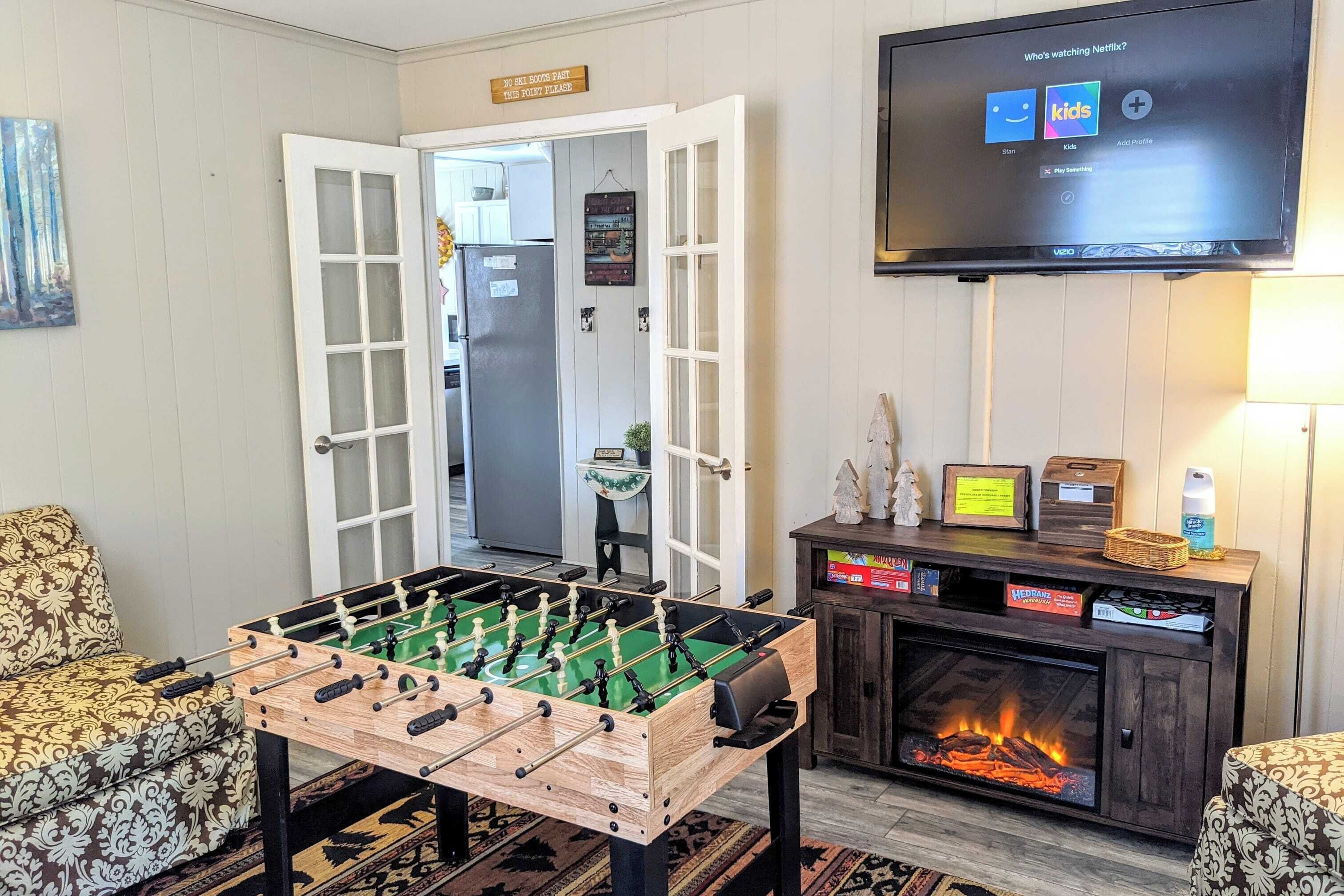 Een knus vertrek met een tafelvoetbaltafel, een open haard en een televisie waarop Netflix-opties te zien zijn.