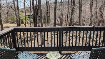 Enjoy the serene forest view from this deck, featuring a small table and two comfortable chairs.