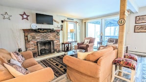 A living room with a brick fireplace, two sofas, a coffee table, and a television mounted on the wall.