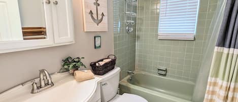 A bathroom with a white sink, a toilet, a shower with a glass door, and a window with blinds.
