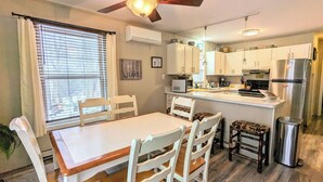 A kitchen with white cabinets, a stainless steel refrigerator, and a dining area with a white table and chairs.