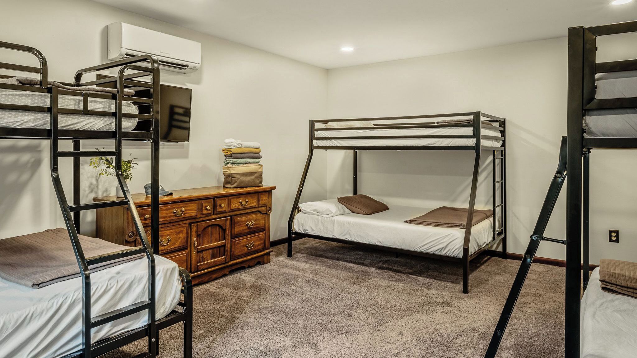 A dormitory room with bunk beds, a dresser, and an air conditioning unit.
