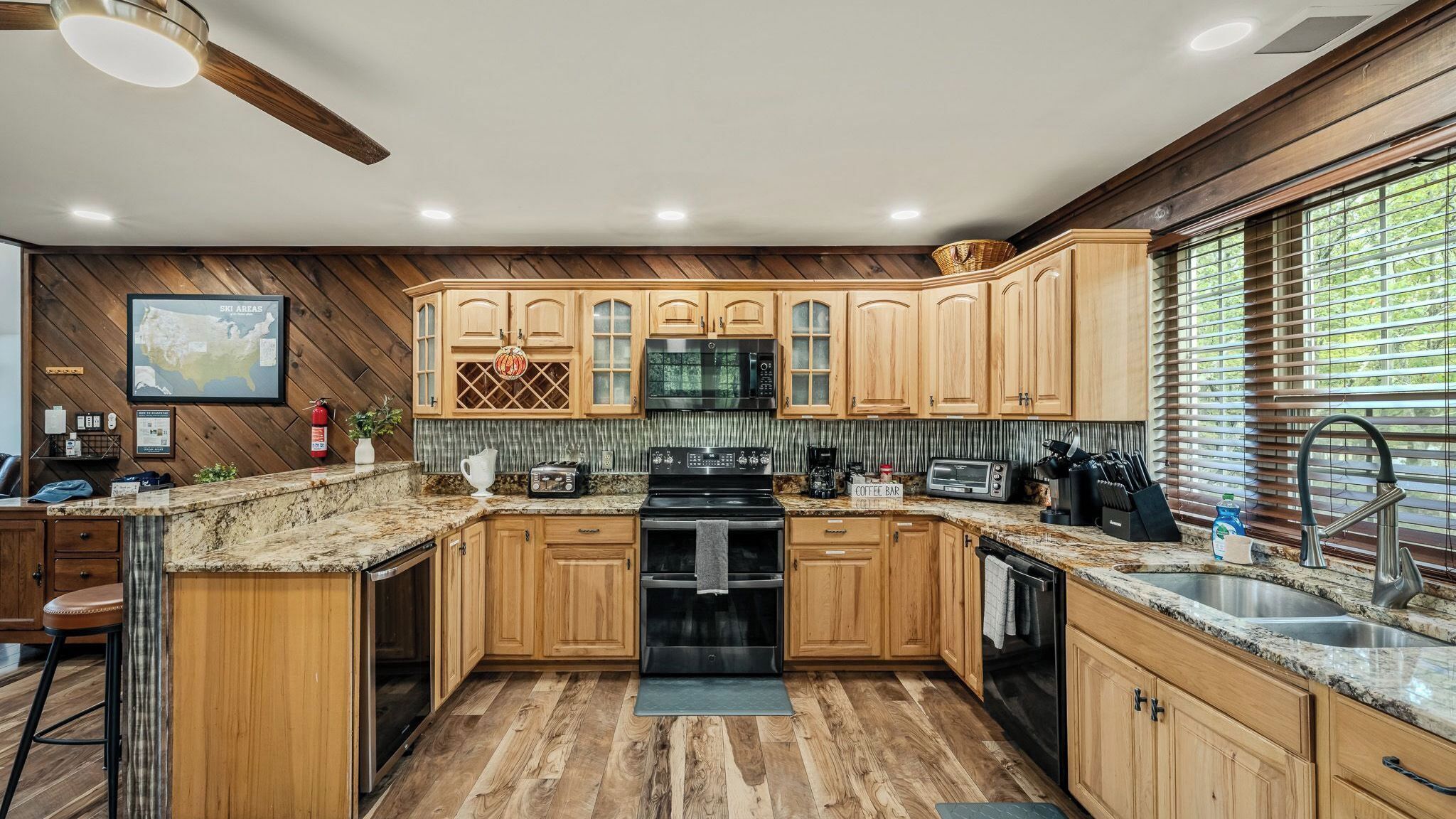A kitchen with wooden cabinets, a microwave, a stove, a coffee bar sign, and a window with blinds.
