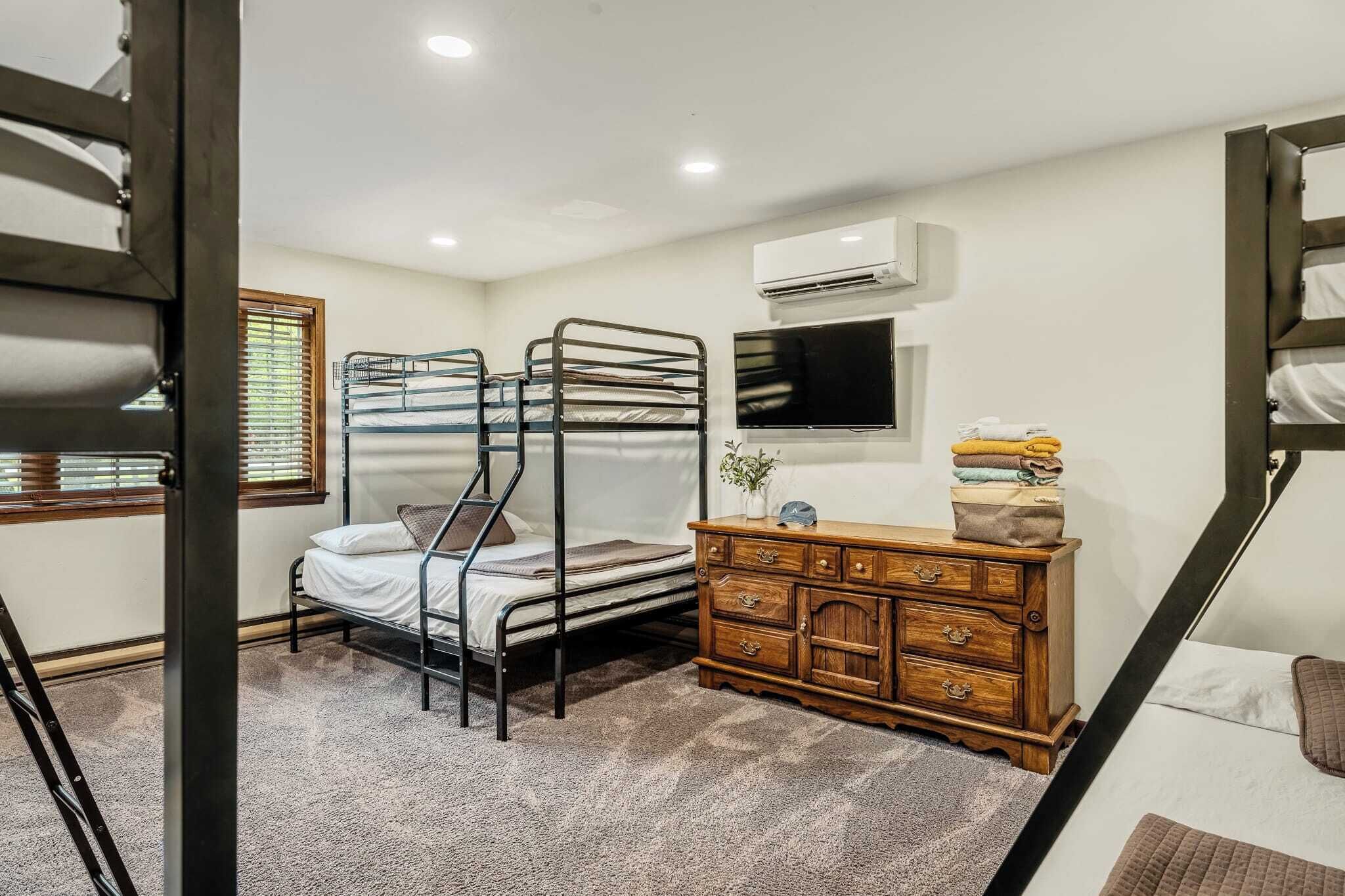 A compact room with bunk beds, a wooden dresser, a flat-screen TV, and an air conditioning unit.