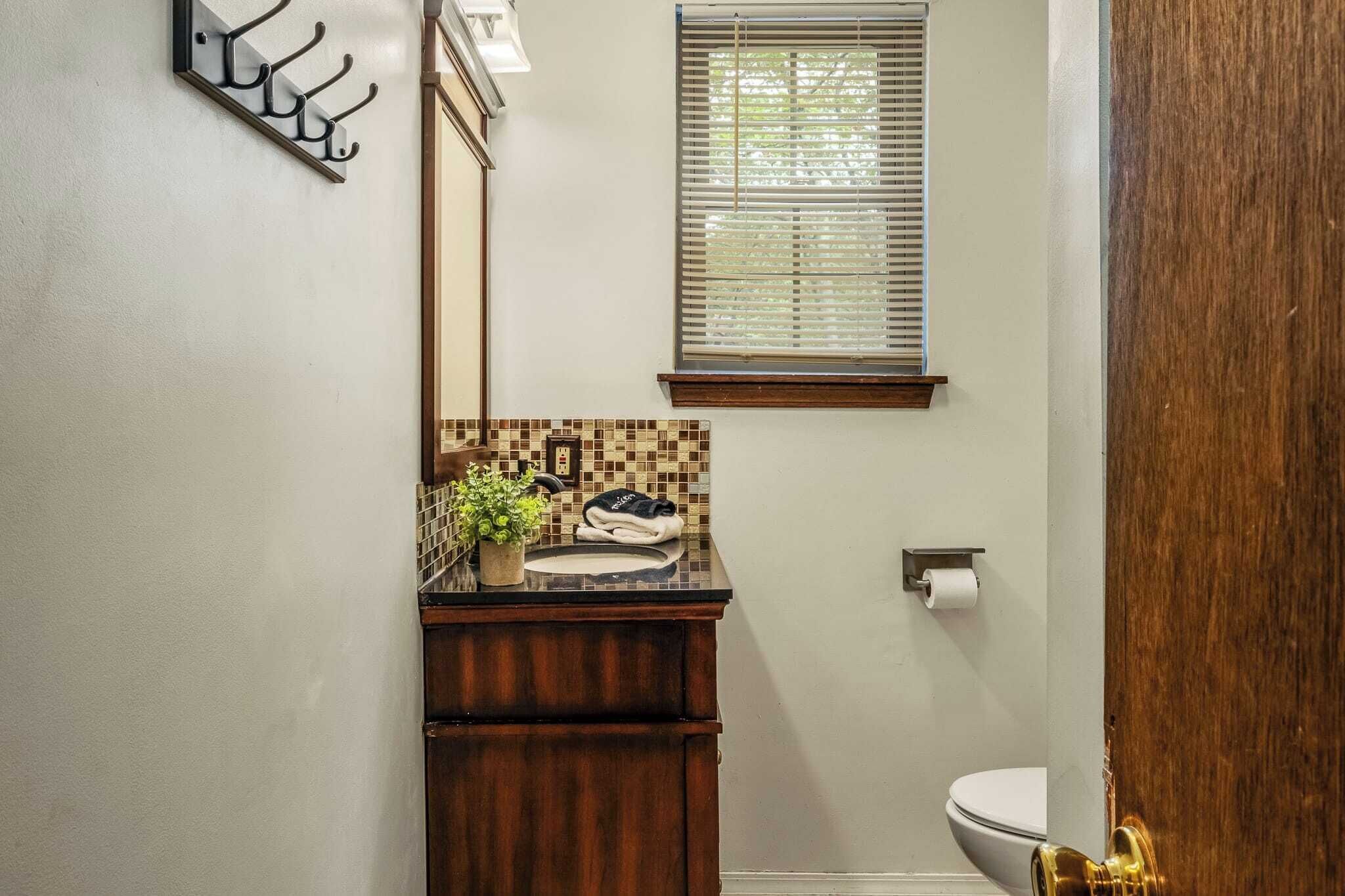 Un bagno con un mobile lavabo in legno, uno schienale piastrellato, una finestra con persiane e un water.