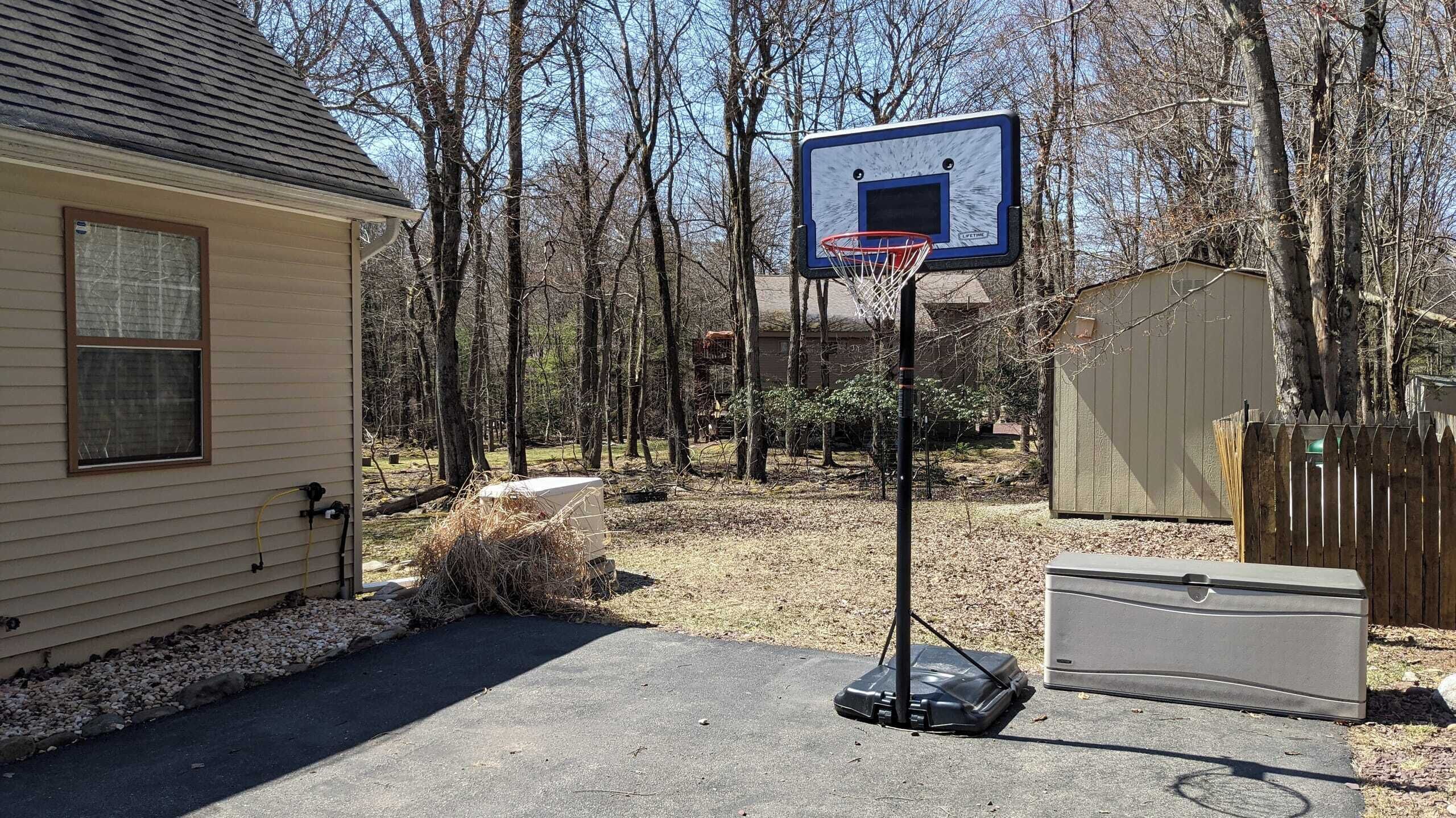 A residential backyard with a basketball hoop, a shed, and a house.