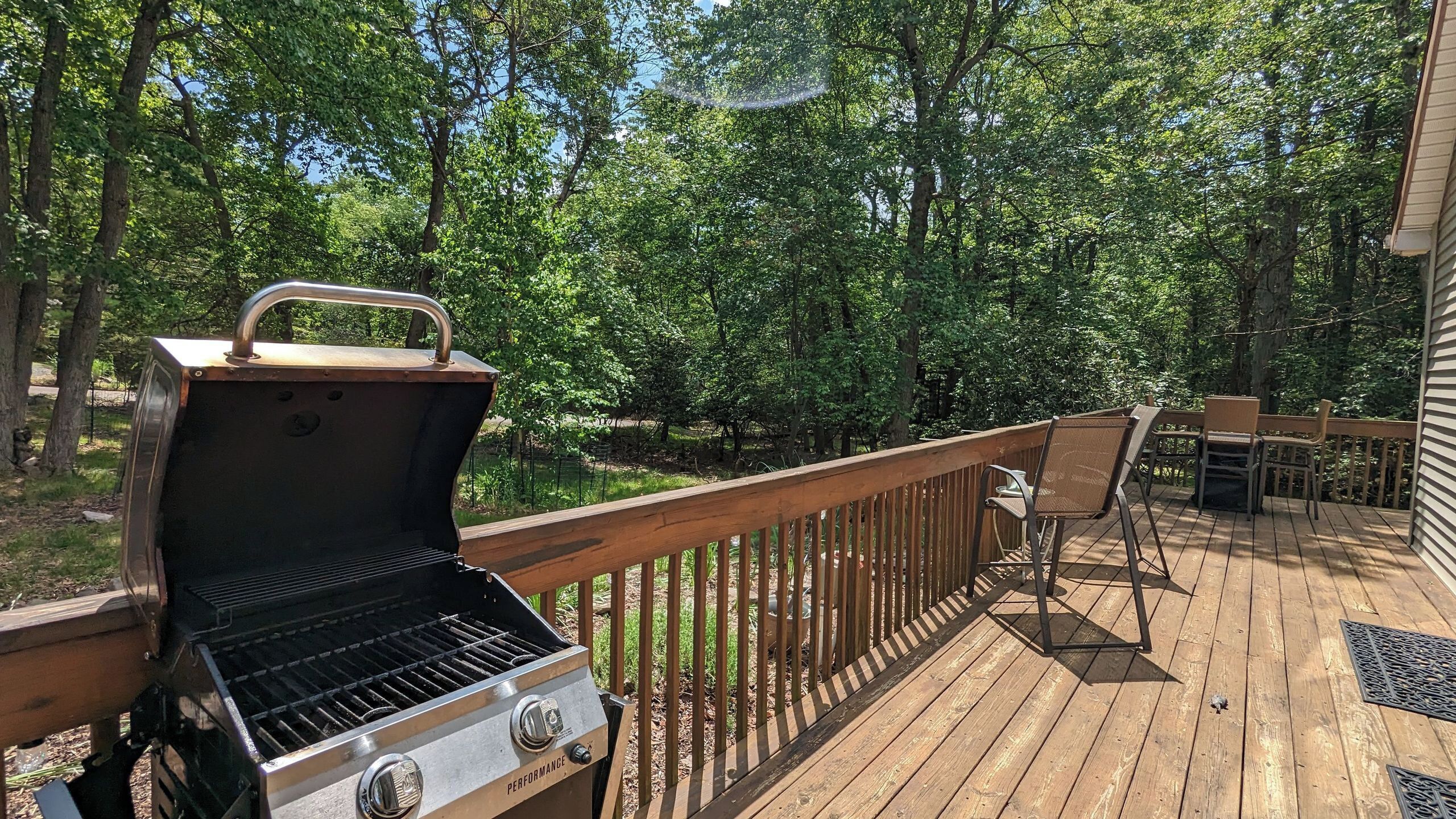 A barbecue grill on a wooden deck with a railing, surrounded by trees.