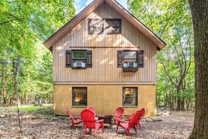 A wooden cabin with a pitched roof, two windows with shutters, and a small patio with red chairs and a table. - Harmony Haven by Avantstay Game Room, Large Deck (Lake Harmony)