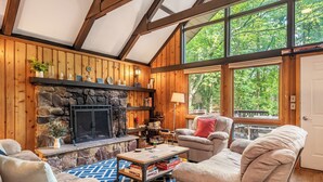 A cozy living room with a stone fireplace, wooden walls, and large windows offering a view of the outdoors. - Harmony Haven by Avantstay Game Room, Large Deck (Lake Harmony)