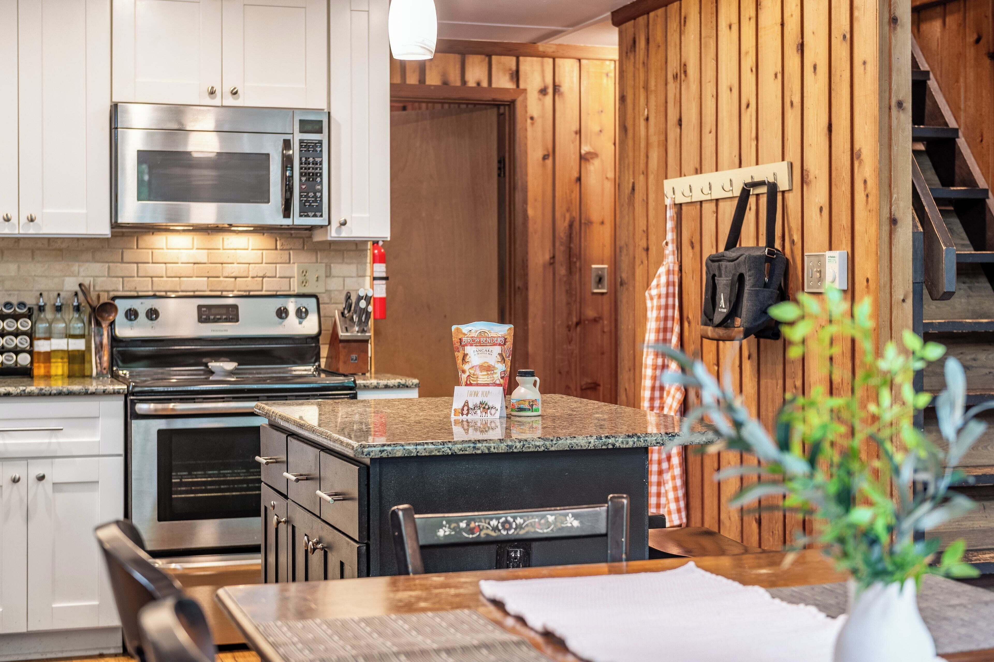 A kitchen with white cabinets, a stainless steel oven, a microwave, and a wooden wall.