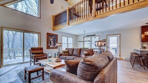 A spacious living room with a large brown leather sofa, wooden coffee table, and a high wooden ceiling with a balcony.