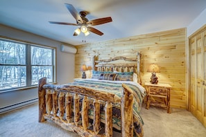 A bedroom with a rustic wooden headboard, a ceiling fan, a large window, and a bedside table with a lamp. - Top Notch Lodge by Avantstay Hot Tub, Game Room, Community Pool, Deck (Albrightsville)