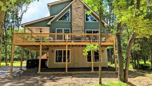 A two-story cabin with a balcony, surrounded by trees.