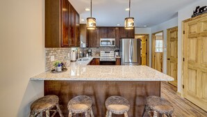 A kitchen with a large island, wooden cabinets, stainless steel appliances, and pendant lighting.