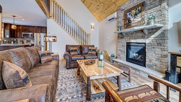 A spacious living area with a stone fireplace, wooden ceiling, and a cozy seating arrangement.