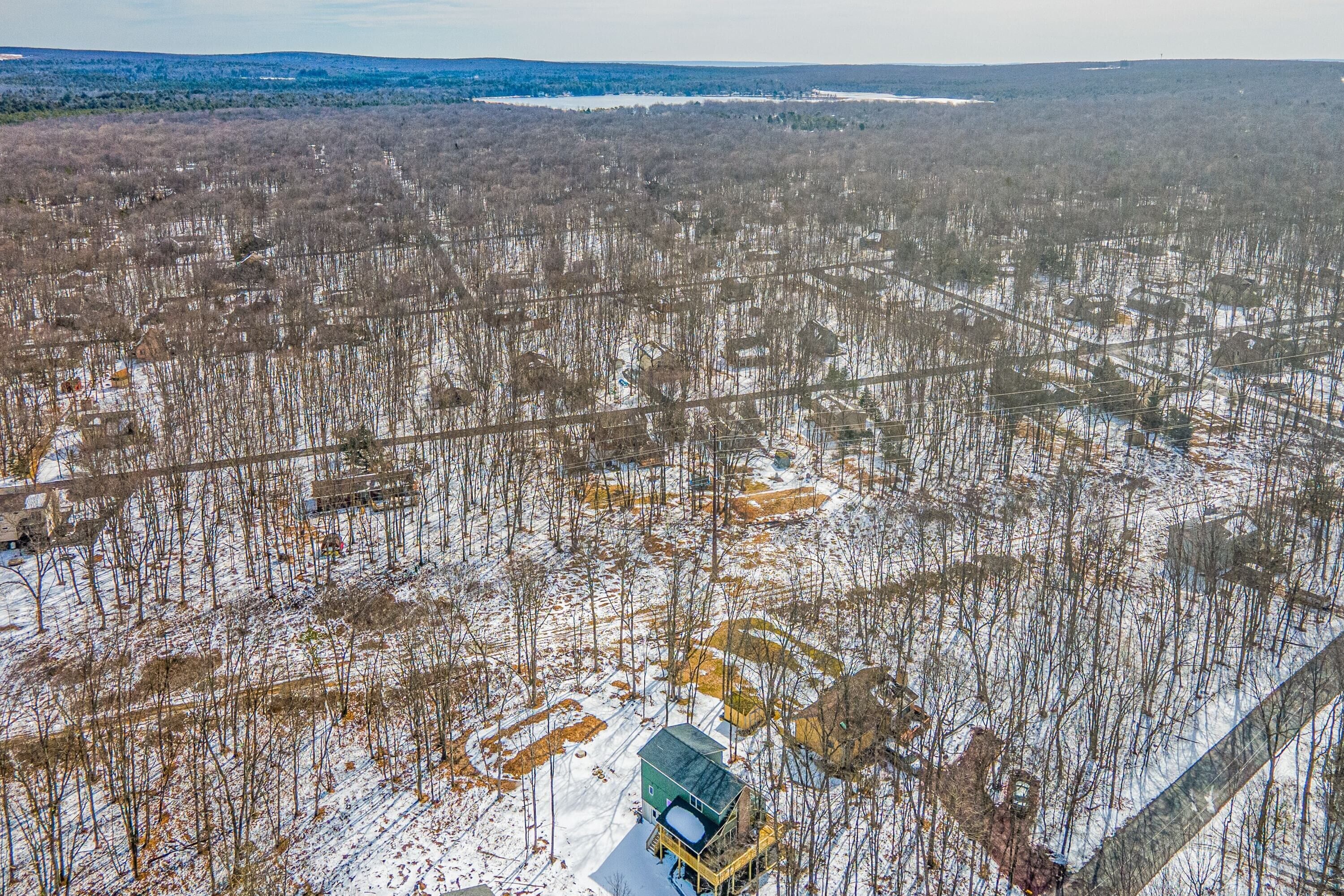 An aerial view of a snowy landscape with a cabin and surrounding forest.