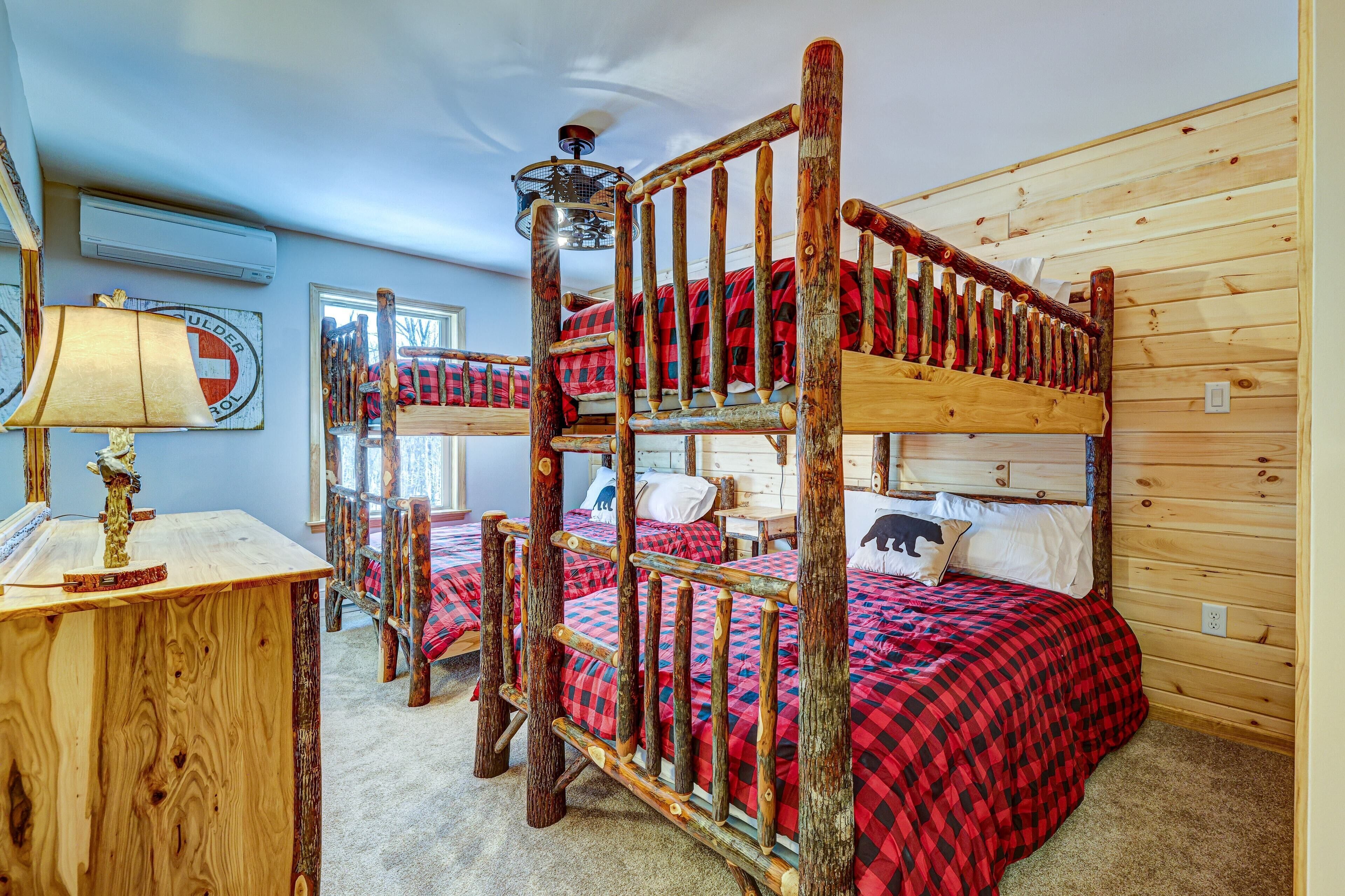 A rustic wooden bunk bed with a red and black checkered bedspread, a wooden desk with a lamp, and a wall-mounted air conditioner.