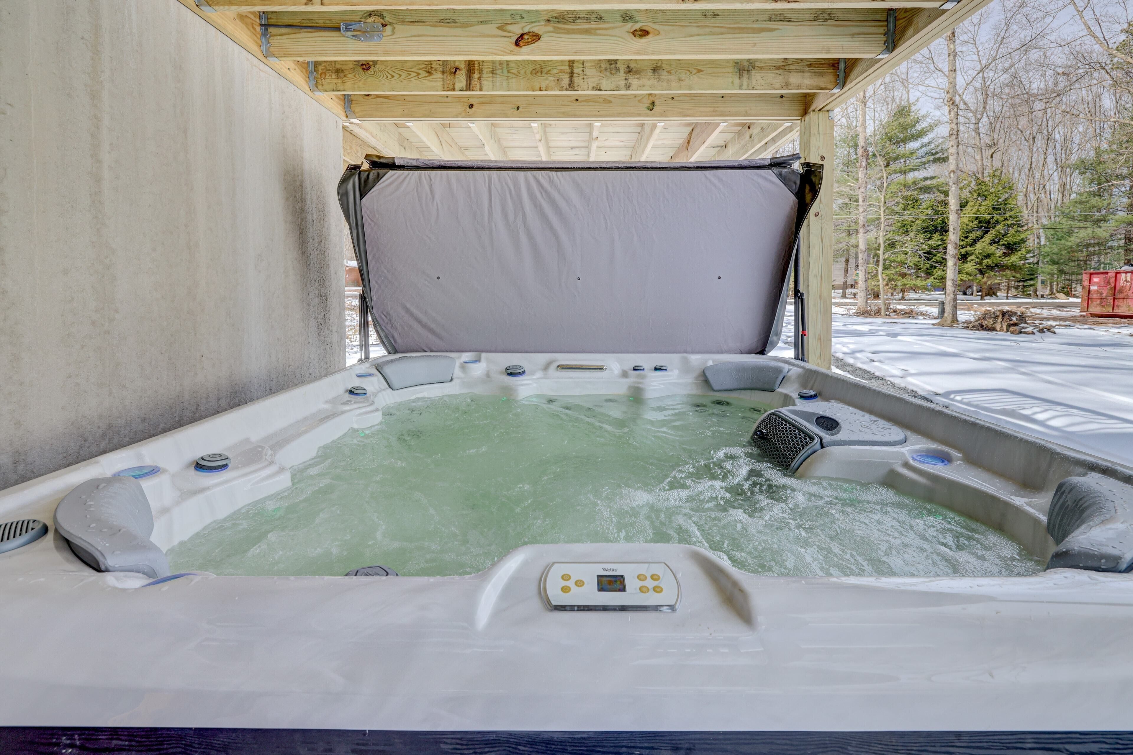 A hot tub with a control panel, surrounded by a wooden deck and concrete walls.