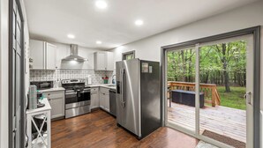 A modern kitchen with stainless steel appliances, a wooden deck, and a view of a forest. - The Tranquil Trails by Avantstay Lake Access, Deck, Fireplace (Albrightsville)