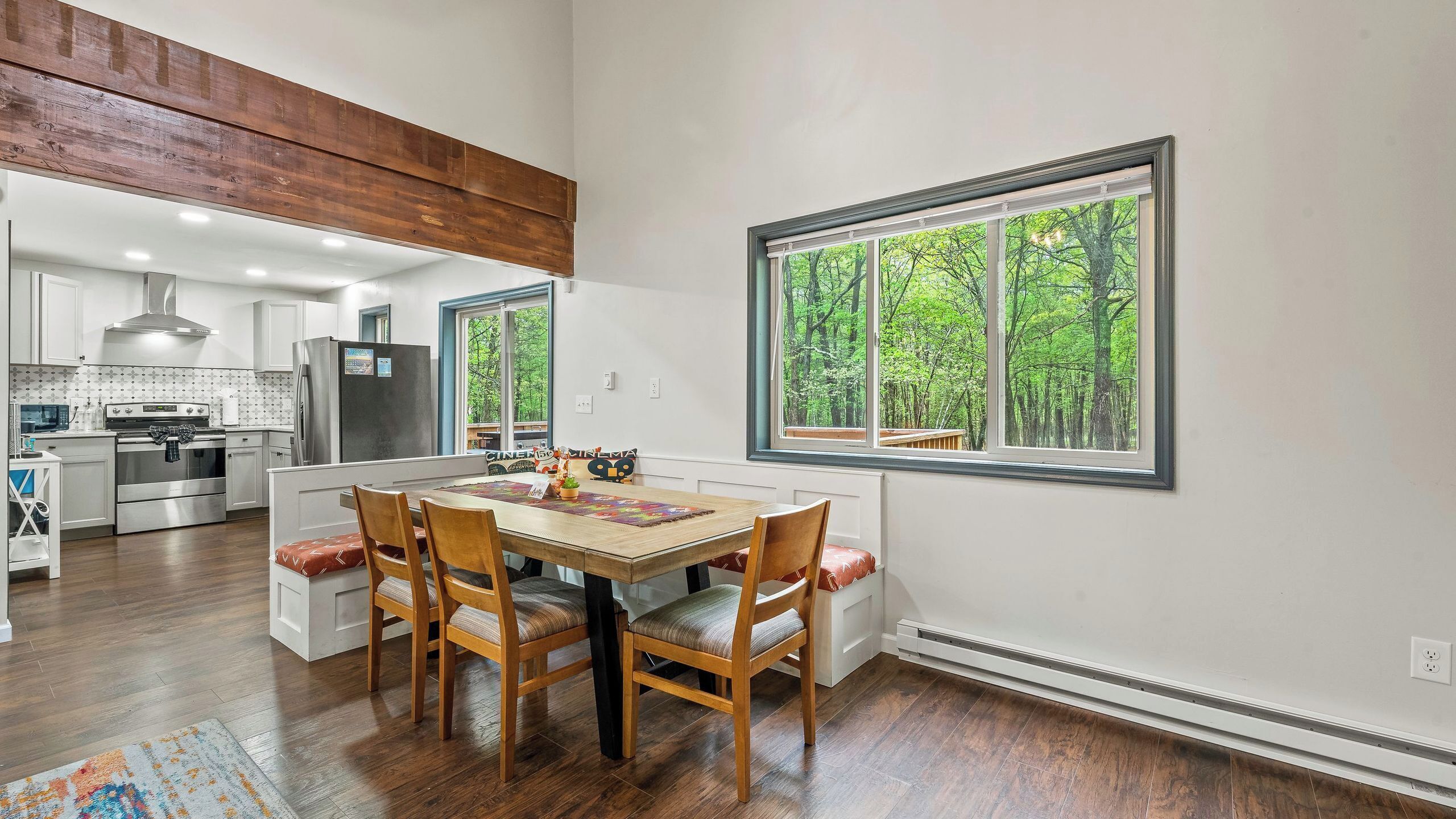 A modern kitchen with white cabinets, a stainless steel refrigerator, and a large window with a forest view.