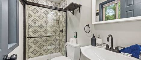 A bathroom with a shower, toilet, sink, and a mirror above the sink.