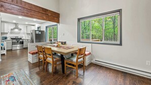 A modern kitchen with a dining area, wooden flooring, and large windows with a forest view. - The Tranquil Trails by Avantstay Lake Access, Deck, Fireplace (Albrightsville)