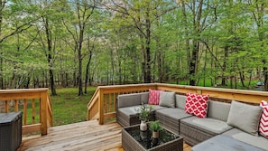 Une terrasse avec un canapé et une table, entourée d’une forêt.