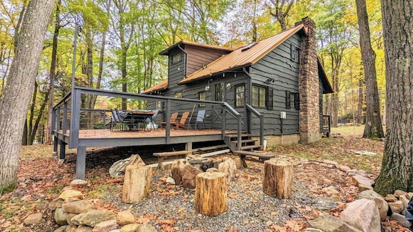 A cabin with a deck, outdoor seating, and a stone fireplace.