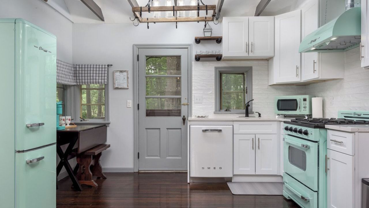A kitchen with white cabinets, a teal refrigerator, a microwave, and a stove.