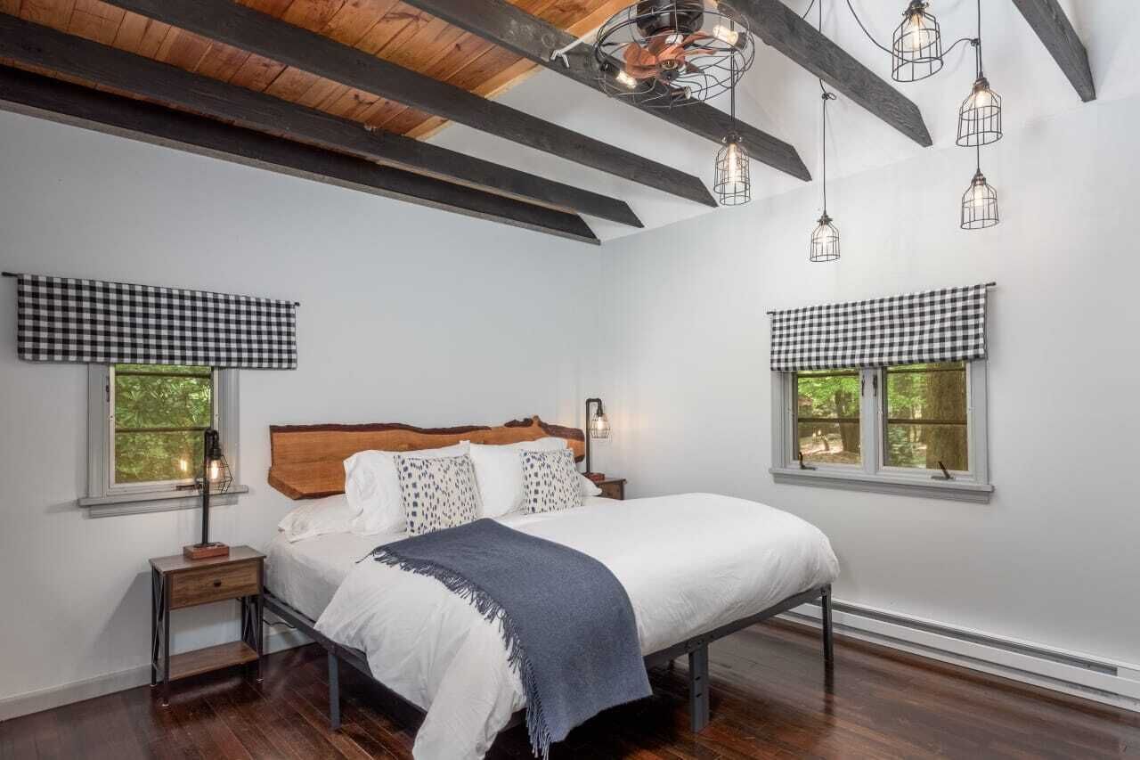 A bedroom with a wooden bed, checkered window valances, and exposed wooden beams on the ceiling.
