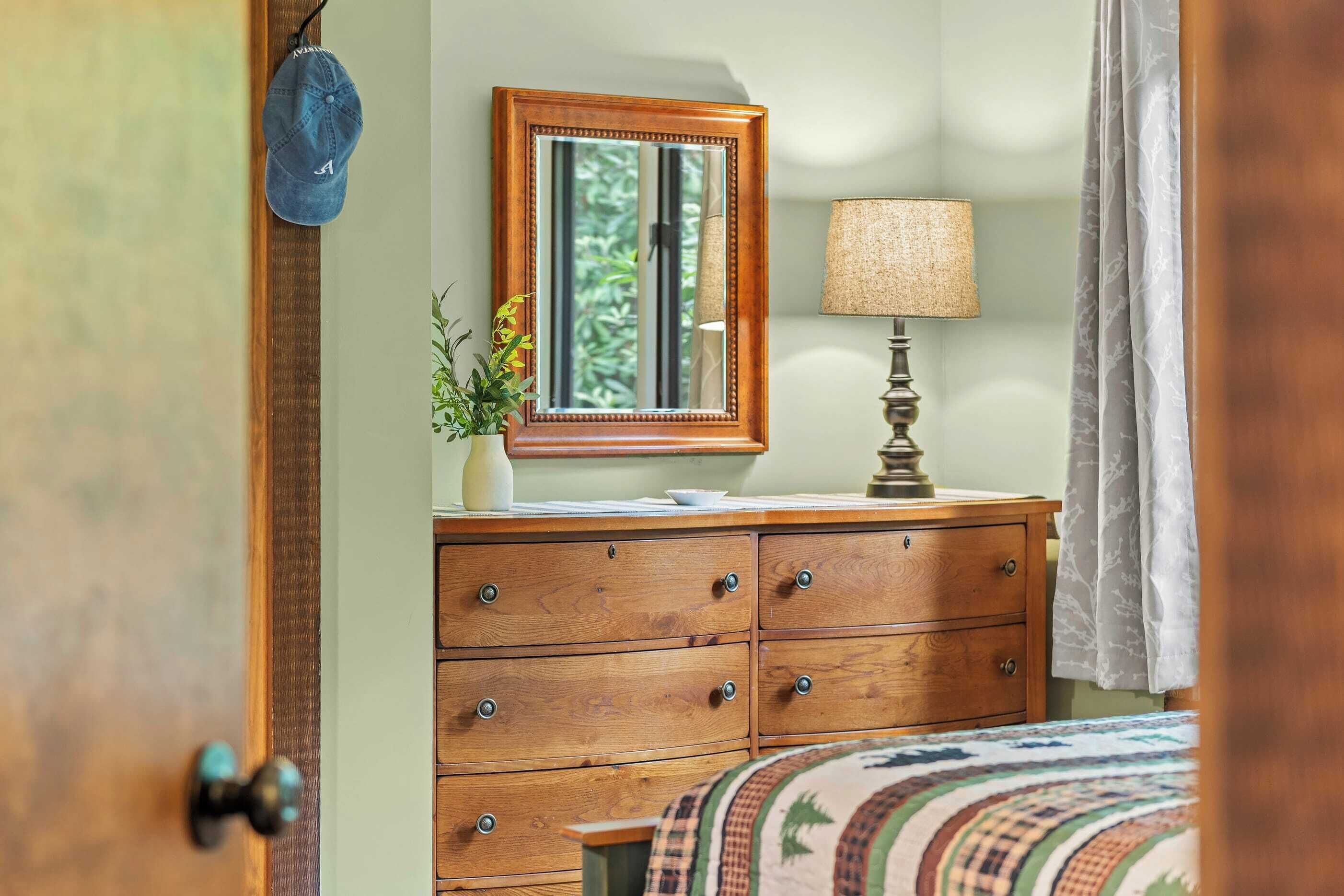 A wooden dresser with a mirror, a lamp, and a plant.