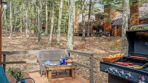 A deck with a grill, a wicker chair, and a table with food items.
